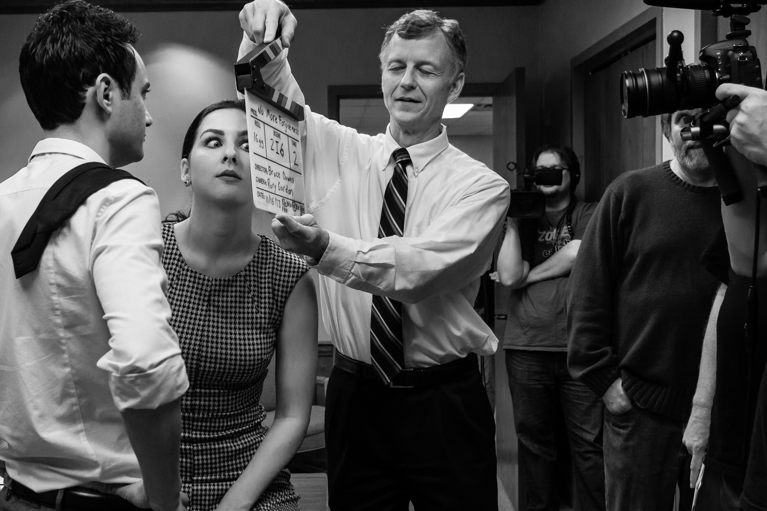 On a film set, an actress pulls a face beside the slate while the crew films