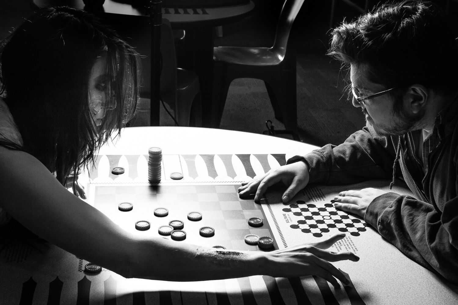 The author plays a board game across a table with an actress in ghost makeup, in dramatic light