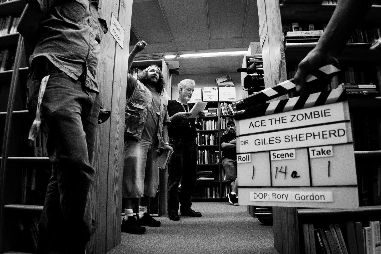 The Ace the Zombie slate held up in a used bookstore, cast and crew crowded between the shelves